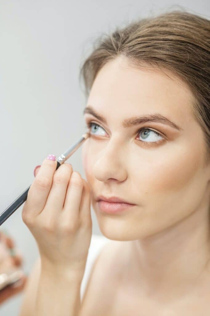 Visagist maakt make-up voor een meisje. Breng beige oogschaduw aan. Detailopname. Verticaal